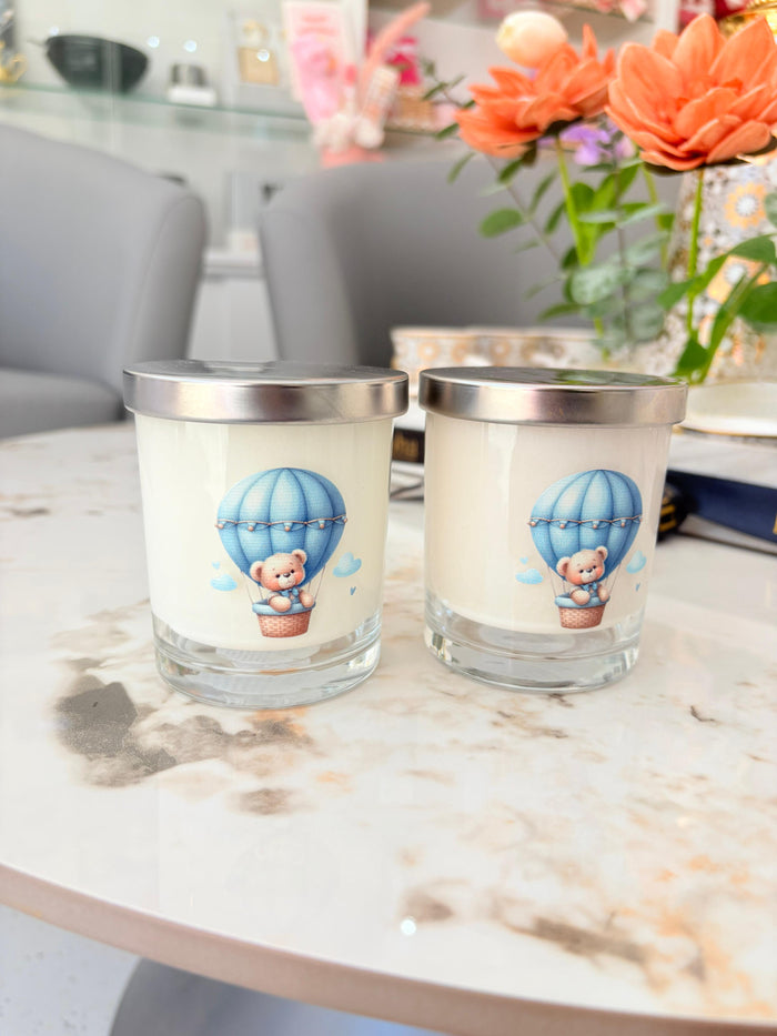 Two glass candles with bear and balloon design on a marble surface.