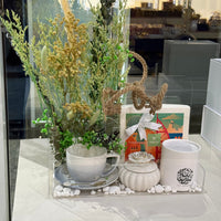Decorative table setting with flowers, candles, and a teapot on a reflective surface.