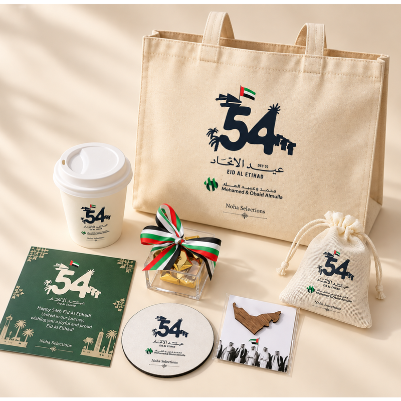 Eid Al Etihad corporate gift set featuring a branded canvas tote bag, coffee tumbler, acrylic chocolate box with UAE flag ribbon, drawstring pouch, greeting card, desk coaster, and a wooden UAE map badge by Noha Selections