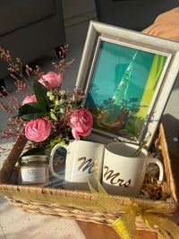Gift basket with 'Mr' and 'Mrs' mugs, flowers, and a framed picture.