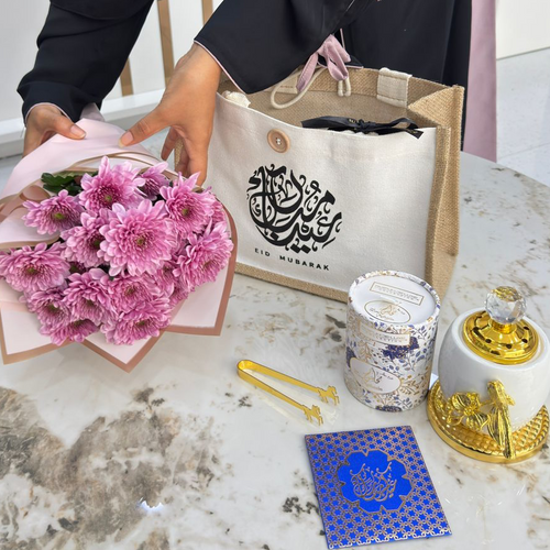 Person holding a bouquet of pink flowers next to a white bag with Arabic text on a marble table.