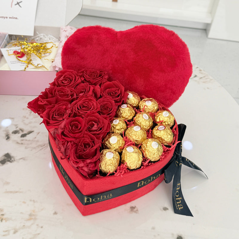 Heart-shaped box with red roses and gold Ferrero Rocher chocolates on a white surface. dubai noha selections 
