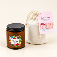 An amber glass candle jar with a black screw lid next to a woven fabric pouch and a pink Teacher's Day card.