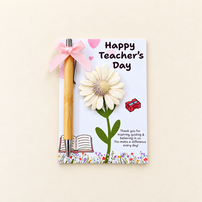 A Teacher's Day greeting card with a bamboo pen tied to it with a pink ribbon. The card features a large white daisy flower, a small red gift box, and the text 'Happy Teacher's Day' on a light cream background.