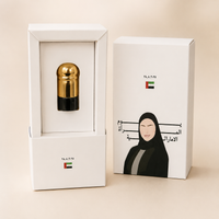 A luxury product presentation featuring a gold and black capsule-shaped item inside a white box, alongside its white packaging box decorated with an illustration of a woman in a black headscarf and Arabic text, and a small UAE flag.