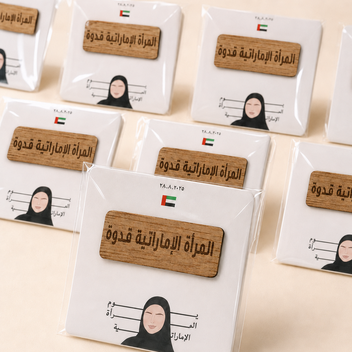A set of square white cards or labels in clear plastic packaging, each with a small wooden plaque featuring Arabic text and a simple illustration of a woman in a black hijab. Multiple identical packs are arranged on a light beige background.