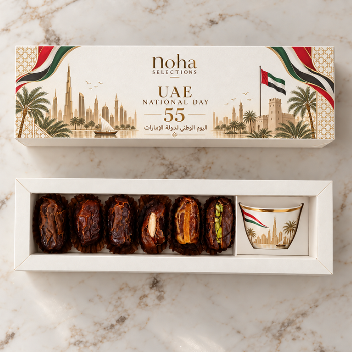 A boxed set of dates and a small cup of tea presented on a white tray, with the outer packaging above showing UAE National Day 55 artwork and the Noha Collection branding. The scene is styled on a light marble surface.