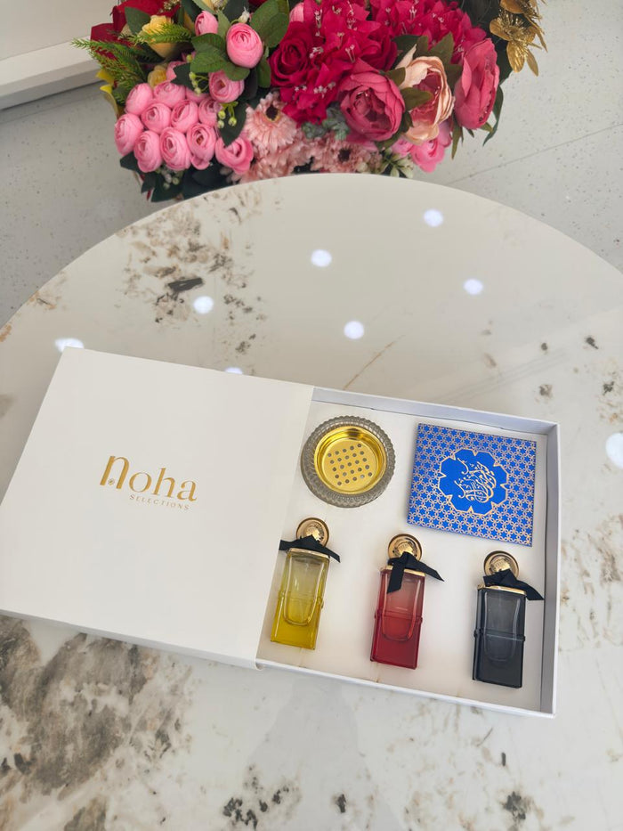 Set of three perfume bottles with a decorative box labeled  on a marble surface with flowers in the background.