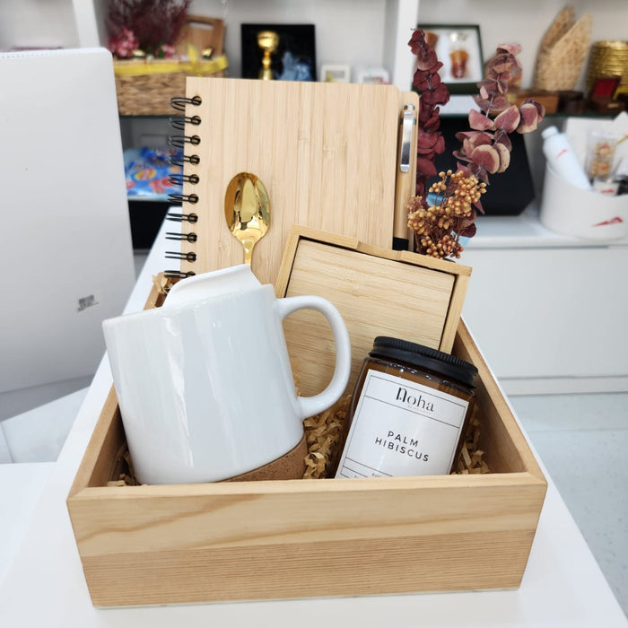 Wooden gift box with a white mug, notebook, and coffee beans on a desk.