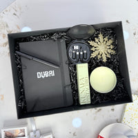 Gift box with stationery items including a pen and a small plant, on a decorative surface.