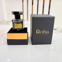 A perfume bottle with a black cap and gold-toned liquid, displayed next to its black presentation box and outer packaging box. The brand name 'noha selections' is printed in gold on the black box.